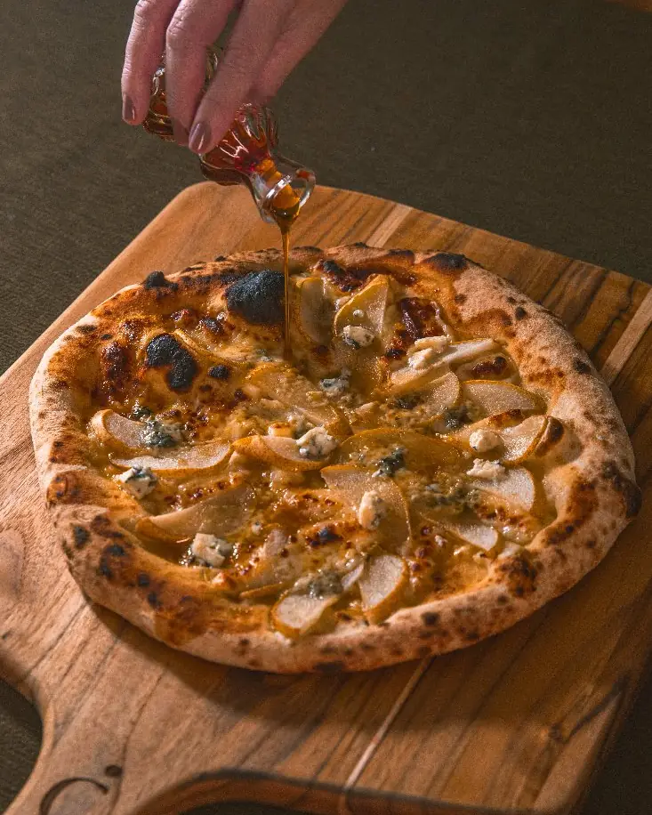 Pizza napolitana Pera con miele da Casapri recebendo fio de mel sobre pá de madeira